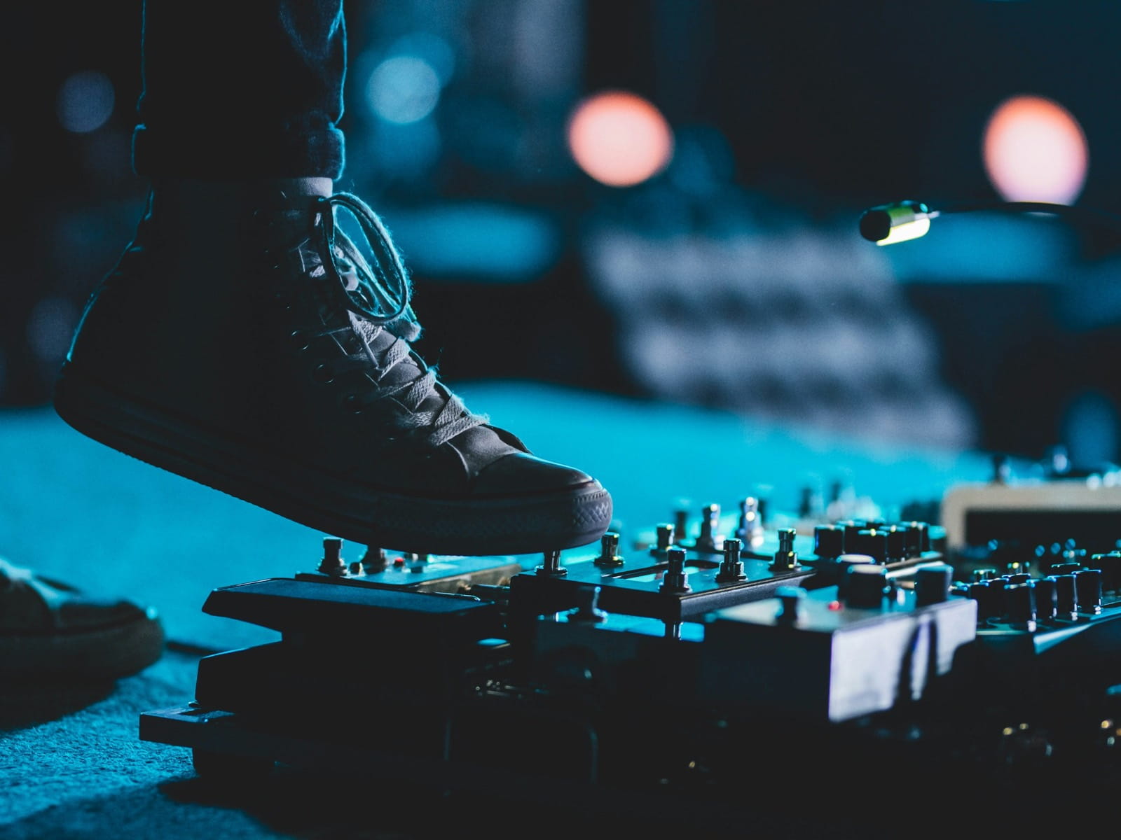 A musician's foot on a guitar effects pedalboard on a blue-lit stage