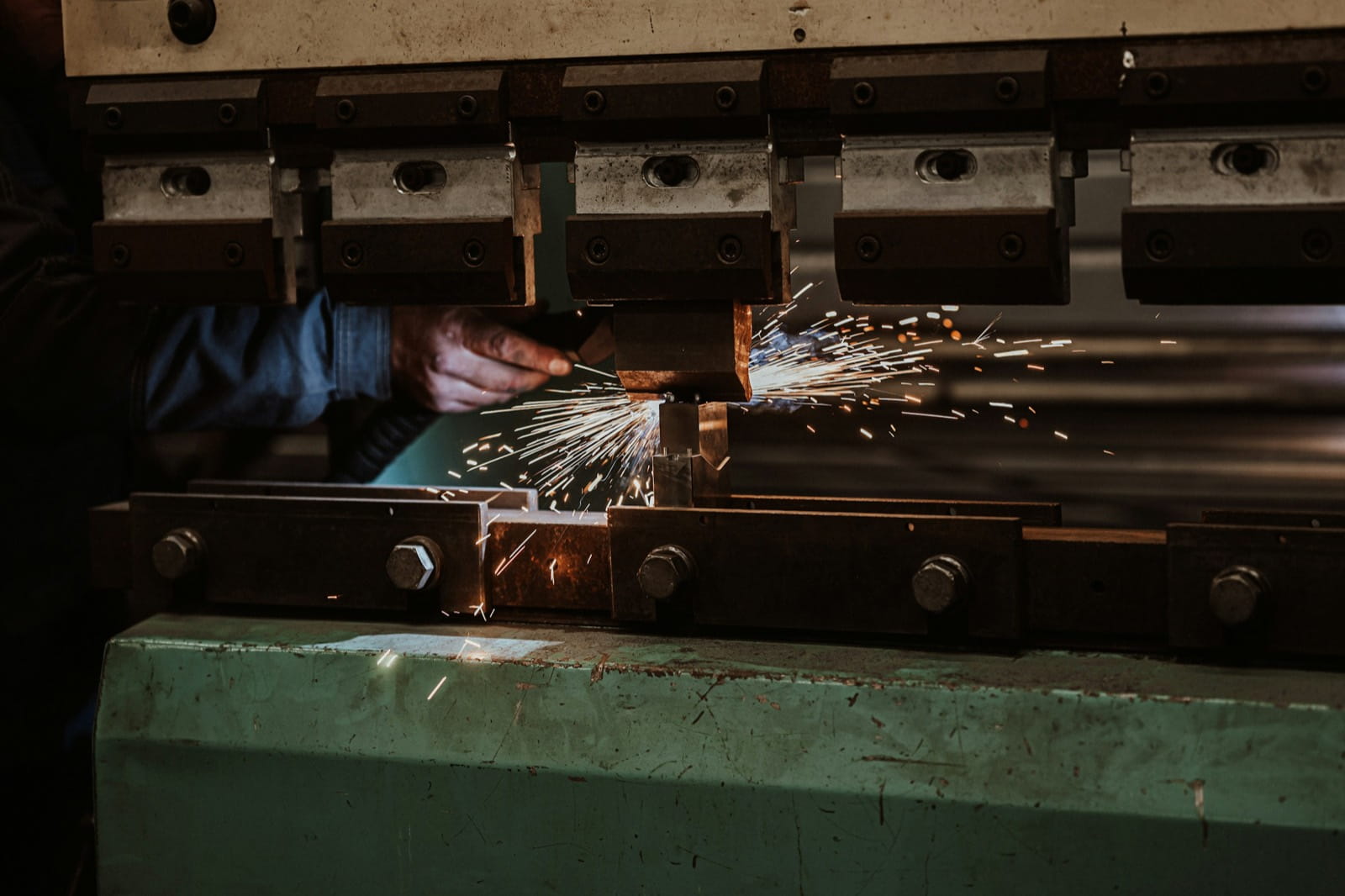 Sparks flying from a press brake as a worker bends steel in a fabrication workshop
