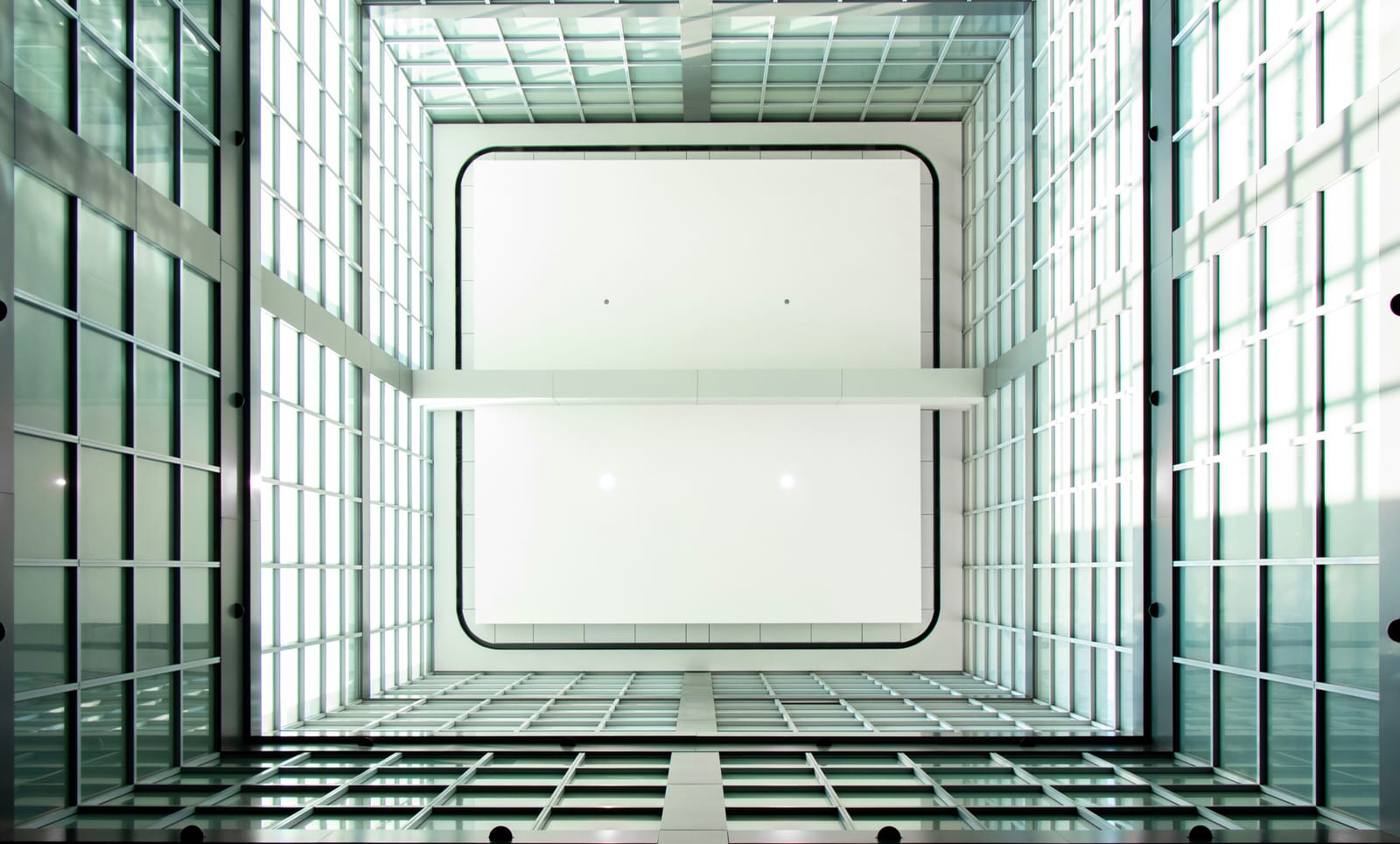 Looking up inside a glass-walled office atrium, geometric glass and steel