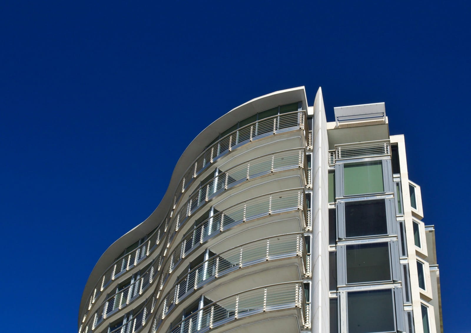 A curved modern apartment tower with wave-shaped balconies against a clear blue sky