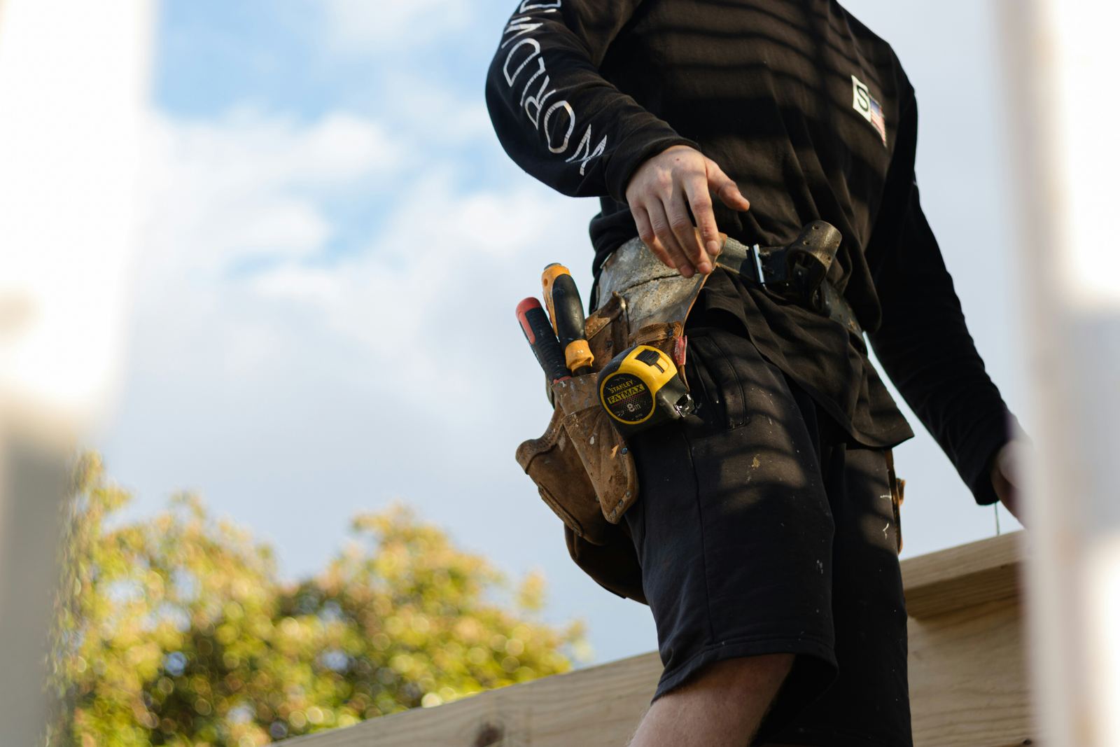 Tradesperson on site wearing a leather tool belt with a tape measure and screwdrivers
